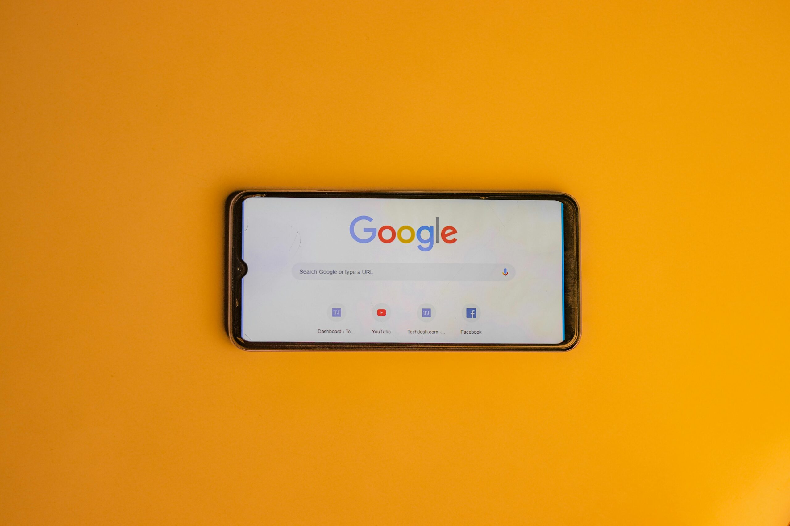 Smartphone displaying Google search page on a vibrant yellow background.