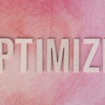 Creative display of the word 'OPTIMIZE' on a pink textured surface.