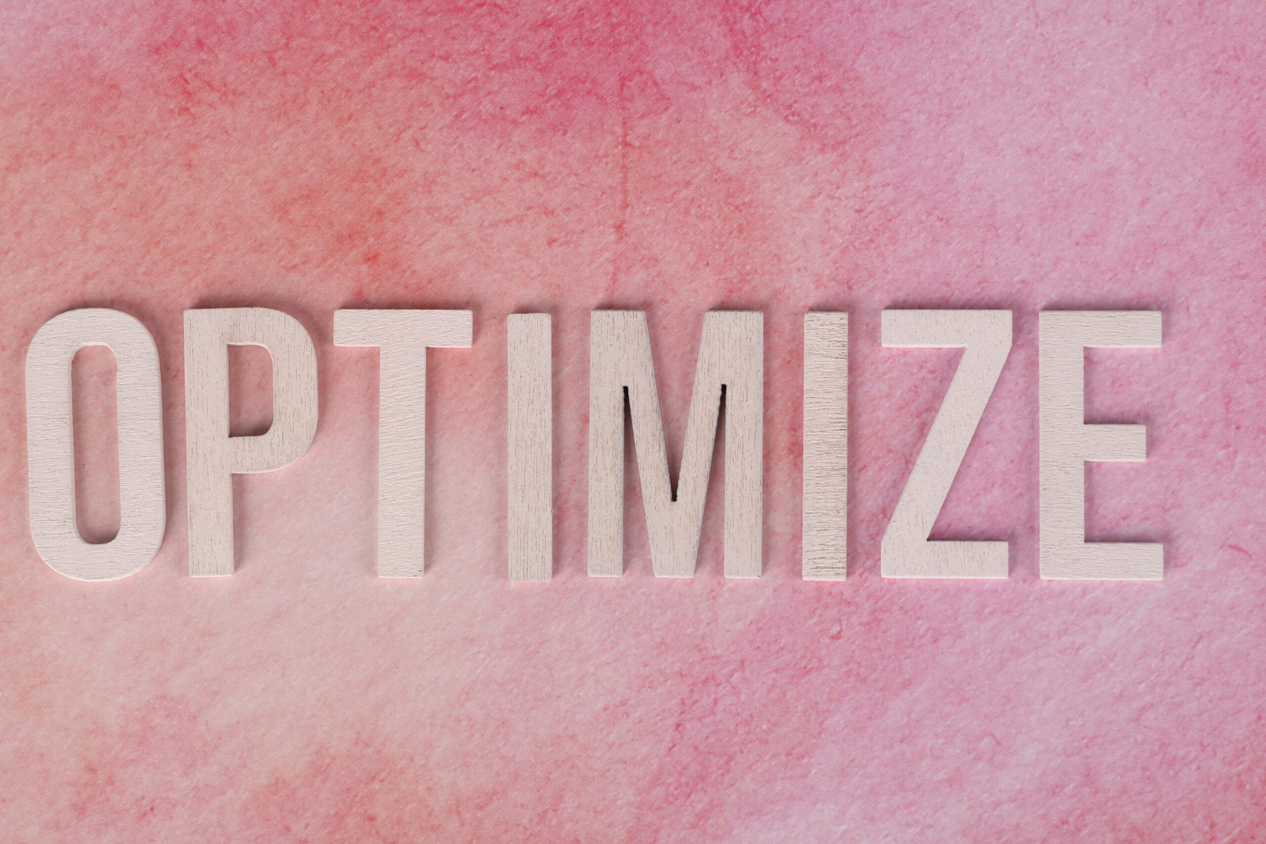 Creative display of the word 'OPTIMIZE' on a pink textured surface.