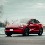 Red electric car parked outdoors, showcasing sleek design amidst winter scenery.