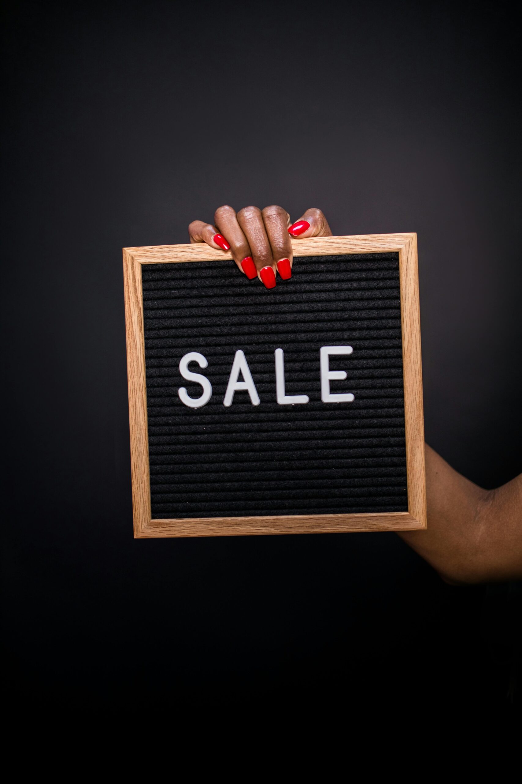 Close-up of a hand with red nails holding a SALE sign on black felt board.