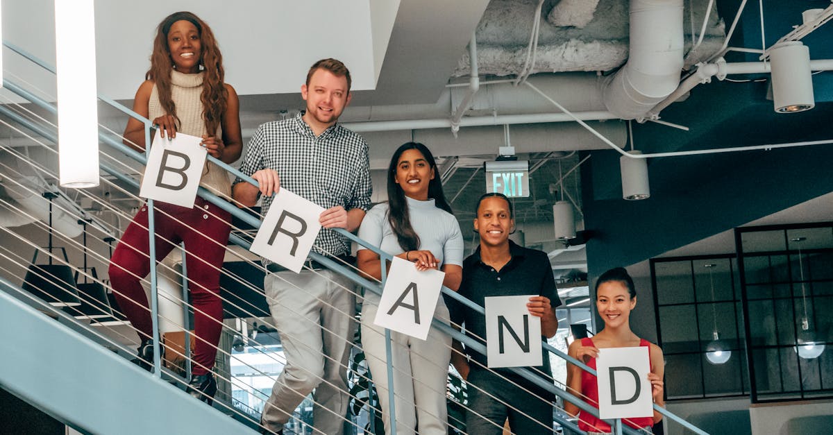 Diverse group of adults smiling and holding 'BRAND' signs on an office staircase.